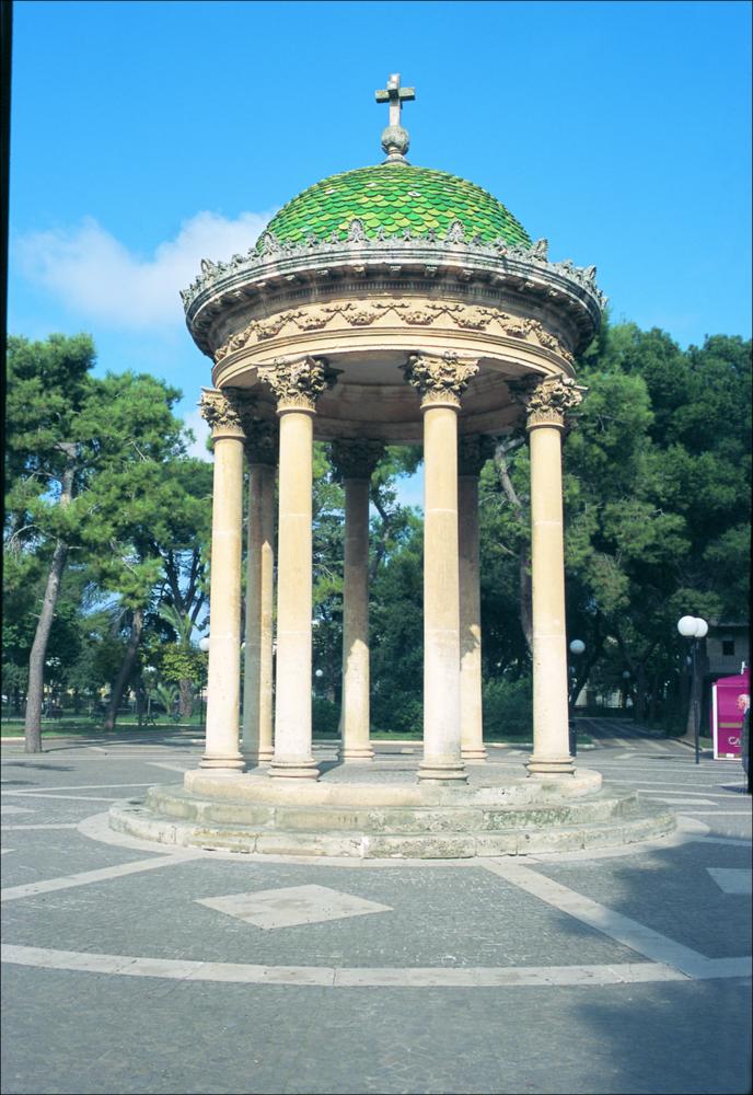 La fotografia è parte della ricca raccolta fotografica “Puglia per tutte le Stagioni” vol. 2, prodotta dall'Assessorato al Turismo e Industria Alberghiera della Regione Puglia, per raccontare la Puglia attraverso immagini suddivise in 5 settori principali: Città e Paesi, Settimana Santa, Territorio, Feste – Sagre – Tradizioni, Mercati – Prodotti – Cucina. L'immagine digitale raffigura l'ottocentesco tempietto circolare della villa comunale di Lecce. Le “ville comunali” della Puglia, realizzate a partire dalla prima metà del sec. XIX, entrano a far parte della progettazione urbanistica dei nuovi borghi ottocenteschi pugliesi. Sorte ai margini dei centri abitati, costituiscono il collegamento tra il vecchio centro storico e il nuovo borgo. La “villa comunale”, tipologia d...