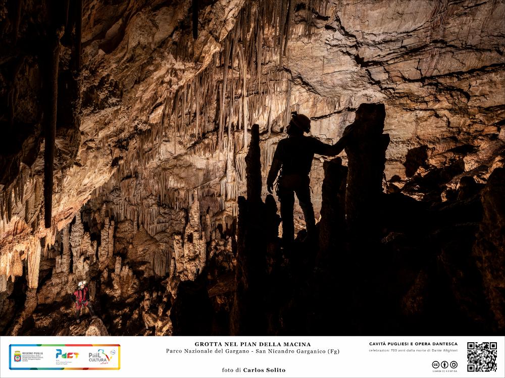 La fotografia ritrae una sala della grotta molto articolata per la presenza di stalagmiti, colonne e formazioni a canne d’organo, che rendono l’ambiente misterioso come fosse l'interno di una mistica basilica.
La grotta si trova in località Pian della Macina a circa 200 metri di altitudine, sulla sommità di Coppa del Mortaio, una delle alture poste a sud della laguna di Lesina.
L’immagine digitale fa parte della raccolta di fotografie prodotte da Carlos Solito per il Progetto digitale “Sillabario sotterraneo – Viaggio dantesco nelle Grotte di Puglia” – realizzato nell’ambito della LEGGE REGIONALE 30 dicembre 2020 - art. 39 “Cavità pugliesi e opera dantesca - Celebrazioni 700 anni dalla morte di Dante Alighieri”.
