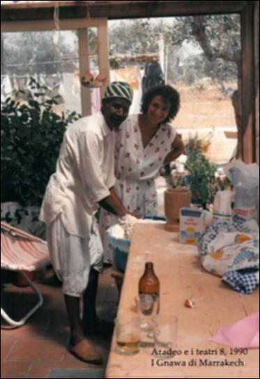 La fotografia in bianco e nero è un momento di vita conviviale, catturato durante l'edizione ottava di "Aradeo e i Teatri", un appuntamento con il teatro sperimentale che la compagnia Koreja, nata nel 1983 nel piccolo borgo salentino di Aradeo, porta avanti sin dall'anno della sua fondazione. Nel segno della contaminazione culturale e teatrale, fulcro e obiettivo di tutto il festival, l'edizione del 1990 si aprì con uno spettacolo di musica e danza dal sapore mediterraneo interpretato dalla comunità "Gnawa" proveniente dal Marrakech, una confraternita religiosa dedita all'animismo e all'Islam, che si integrò alla comunità di Koreja, con la quale condivisero cultura, rituali e tradizioni, anche a tavola.