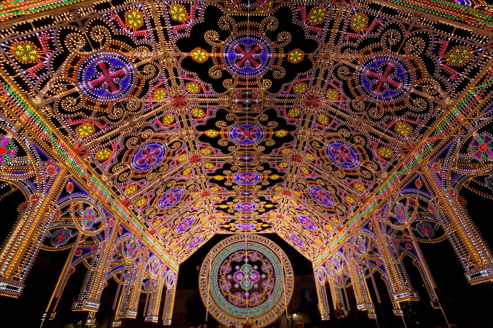 Lo scatto fotografico immortala l’allestimento del borgo di Melendugno, in occasione dei festeggiamenti in onore del Santo Patrono Niceta, con luminarie dai colori sfavillanti: lo spettacolo è estremamente suggestivo.
La Festa Patronale di San Niceta Goto Martire, istituita nel 1740, si celebra nei giorni 15 e 16 Settembre a Melendugno in provincia di Lecce. Il rito religioso parte nove giorni prima della Festa, con delle celebrazioni eucaristiche presso la chiesa Madre e in forma esclusiva viene celebrata la santa messa in rito bizantino presso l’Abbazia di San Niceta situata in Melendugno sin dal 1167, riconosciuta appunto come uno dei più importanti riferimenti storici del territorio.
Il giorno della vigilia della Festa, come da tradizione pluricentenaria, al termine...