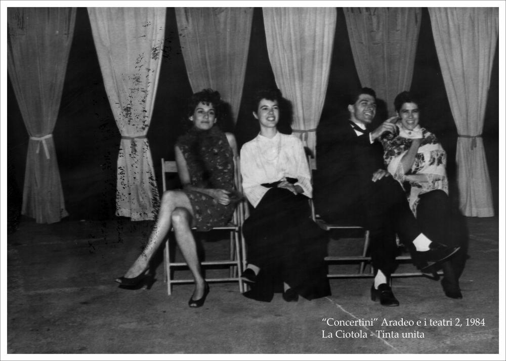 La fotografia in bianco e nero immortala un momento dello spettacolo teatrale “Tinta unita indoor” nell'ambito della rassegna annuale “Aradeo e i Teatri” del 1984, alla seconda edizione con il titolo “Concertini”, un appuntamento con il teatro sperimentale che la compagnia Koreja nata nel 1983 nel piccolo borgo salentino di Aradeo portò avanti sin dall'anno della sua fondazione. Lo spettacolo è messo in scena, nella piazzetta San Giovanni, dalla compagnia teatrale La ciotola di Verona, nata nel 1976 dall'incontro tra gli attori del “Libre teatro libre” argentino e alcuni giovani attori di Verona. “Tinta unita”, per la regia dell'attrice argentina Graciela Ferrari che dal 1982 assunse la direzione della compagnia, ha una trama che alterna poesia ed umorismo, gioco e dram...