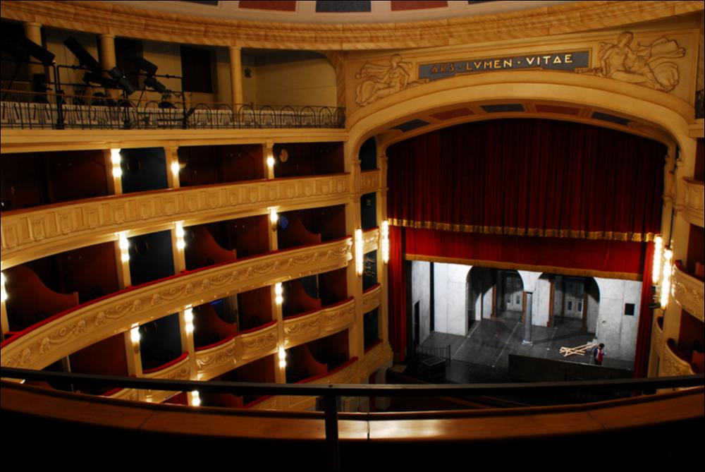 L'immagine è parte della campagna fotografica realizzata dalla fotografa Margherita Mirabella per Teatro Pubblico Pugliese che, con i suoi scatti, ha ripreso le eleganti architetture e i rifiniti dettagli di alcuni dei più bei teatri pugliesi e di alcuni spettacoli teatrali portati in scena in questi ultimi anni. Lo scatto ci restituisce la sala interna del Teatro Comunale "Giuseppe Verdi" di San Severo, riconosciuto come la più grande struttura teatrale di Capitanata e terzo teatro all'italiana più importante di Puglia dopo il Petruzzelli di Bari e il Politeama Greco di Lecce. Il monumento, originariamente denominato teatro Comunale del Littorio, viene progettato dall'architetto Cesare Bazzani rispettando a pieno i canoni stilistici dell'arte fascista. I lavori, inizia...