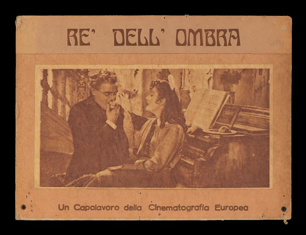 L'immagine riproduce uno dei manifesti conservati presso la Mediateca Regionale Pugliese (vedi Note). Si tratta del soggetto della fotobusta del film "(Il) Re dell'ombra". La produzione italiana di fotobuste negli anni '30 e '40 comprendeva anche quelle realizzate su supporti cartonati di dimensioni particolari, spesso 24x34 cm o più genericamente di 49x34 cm circa. Come vediamo da questo esempio, le fotobuste di questo tipo su cartone (che venivano chiamate di tipo "anteguerra") presentano una fotografia di scena in bianco e nero incollata, qui ritoccata sui colori del seppia. Intorno, nello spazio rimanente, con un'illustrazione autonoma, venivano indicate dal grafico le informazioni principali del film (titolo, generalmente anche regista e attori). In questo caso, in...