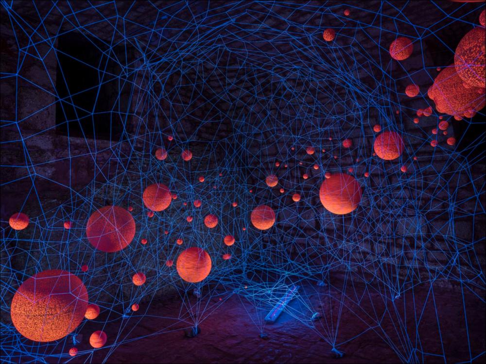 Lo scatto fotografico riprende l’installazione “In Parallel” delle artiste slovene Natalija R. Črnčec e Nina Šulin, collocata presso il Soccorpo della Chiesa Santa Lucia di Alberobello. Un viluppo di solidi geometrici colorati, inseriti in un reticolo di fili luminosi, si intrecciano e reagiscono alla luce ultravioletta. L’opera è stata accompagnata da sonorità tratte da musica ambient sperimentale.
L’installazione è stata realizzata nell’ambito della seconda edizione del Life - Alberobello Light Festival 2017 che ha illuminato il centro cittadino e alcuni dei suoi luoghi più caratteristici dal 30 settembre all’8 ottobre.
Il Festival è organizzato da Lightcones e Agit - Associazione Giovani Imprenditori del Turismo, responsabili rispettivamente della direzione artist...