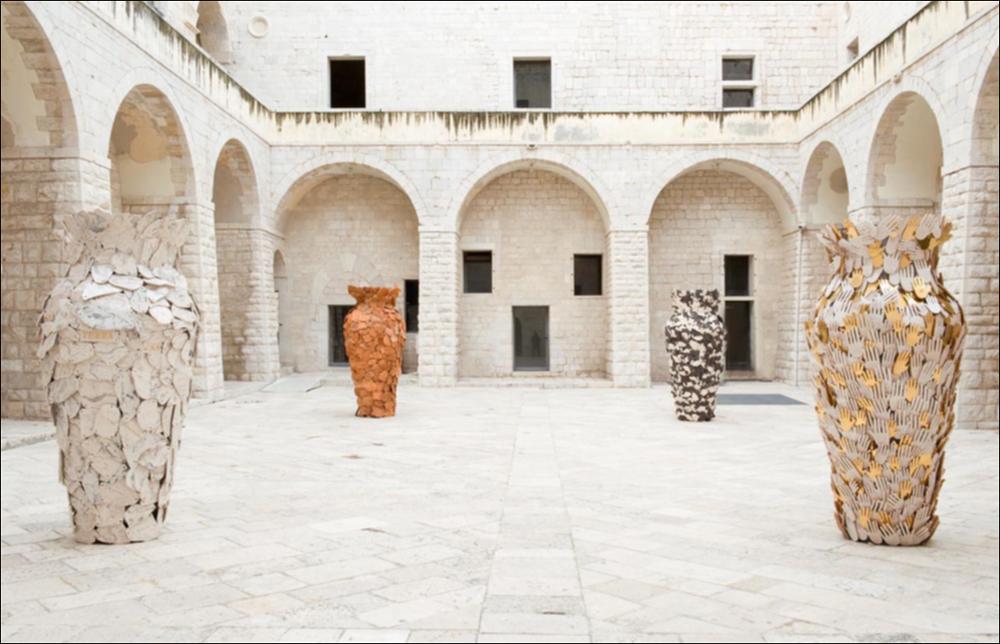 L'immagine digitale in oggetto è stata scattata con luce naturale in occasione della mostra “Le culture sacre dell'Arte” dell'artista pugliese Tarshito, realizzata dal 23 novembre 2008 al 25 gennaio 2009 negli spazi del Castello di Trani. Protagoniste assolute dello scatto sono quattro grandi anfore in metallo rivestite da diversi elementi iconografici realizzate dall'artista tra il 2007 e il 2008. Collocate sui quattro angoli della corte interna del castello, le anfore si presentano tanto possenti da annientare completamente lo spazio esterno dell'architettura che le ospita. All'arte scultorea di Tarshito va riconosciuta una grande forza comunicativa, gli stessi vasi sono pregni di un forte significato intrinseco che l'artista stesso non esita a svelare. Il vuoto all'i...