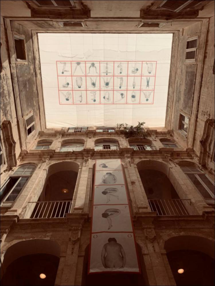Il cortile interno del maestoso Palazzo Palmieri, che si affaccia sulla omonima piazza, è stato ricoperto dalla riproduzione su tela dell’“Alfabeto Poetico Monumentale” dell’artista Tomaso Binga, alter ego maschile di Bianca Pucciarelli, nata a Salerno nel 1931. Tomaso Binga, con la sua ironia e spiazzamento visivo, critica i privilegi del mondo degli uomini. Con Alfabeto poetico monumentale, l'artista rimette in questione, alla metà degli anni Settanta, i modelli estetici, sociali e culturali attraverso cui il corpo femminile era abitualmente rappresentato ed esposto. Con le sue opere il corpo si trasforma da oggetto in lettera, parola, linguaggio assumendo la dignità della scrittura e del messaggio di crescita sociale. Così come i bambini imparano l’alfabeto così la s...