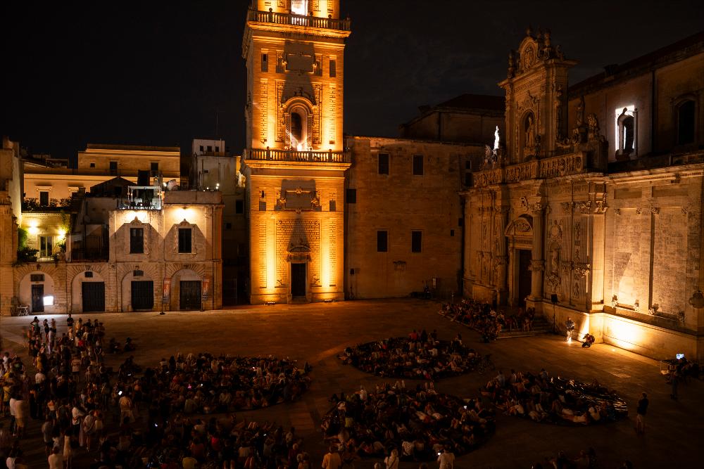 <div>La foto mostra <strong>la piazza di Lecce allestita per lo spettacolo</strong> <em>Vergine madre, figlia del tuo figlio</em> di <strong>Ermanna Montanari</strong>. Scattata dall’alto di sera, la scena evidenzia il pubblico disposto a cerchi, creando un’atmosfera intima e suggestiva nello spazio urbano. Lo spettacolo darà voce al trentatreesimo canto del <em>Paradiso</em> della <em>Divina Commedia</em>, con <strong>sound design di Marco Olivieri</strong> e <strong>luci di Luca Pagliano</strong>, trasformando la piazza in un luogo di meraviglia e partecipazione collettiva.</div>...