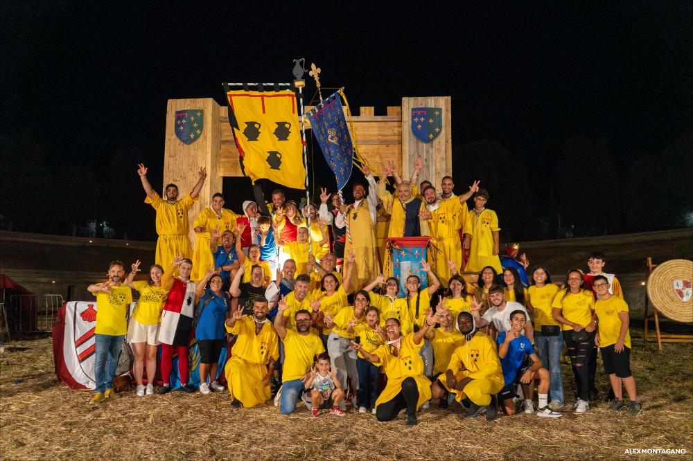 <div>La fotografia documenta la proclamazione del rione vincitore del Torneo delle Chiavi. È raffigurata <strong>Porta Foggia</strong>, con la squadra schierata in abiti storici e nei colori identificativi del rione. In evidenza lo stendardo della vittoria, recante il simbolo delle Chiavi, emblema della competizione. L’immagine testimonia uno dei momenti conclusivi e più rappresentativi della Settimana Medioevale di Lucera, rievocazione storica di rilievo per la tradizione cittadina.</div><div><br></div><div>Il <strong>Torneo delle Chiavi </strong>rappresenta uno dei momenti più identitari e attesi della Settimana Medioevale di Lucera, nonché uno degli eventi simbolo della tradizione cittadina. Inserito nel programma delle celebrazioni 2025, il...