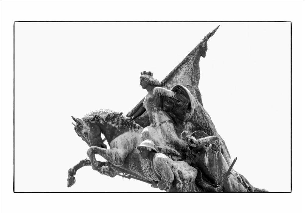 L'immagine digitale mostra un particolare del Monumento ai Caduti a Gravina in Puglia, opera dello scultore Angelo Galli, sito nella Villa Comunale. Protagonista assoluta della maestosa opera bronzea, è la donna, personificazione dell'Italia, in sella ad un cavallo immortalato nell'atto di impennarsi. In basso, ai lati del cavallo sono presenti dei soldati armati, scolpiti nel momento che precede la carica durante il combattimento, si può notare infatti come un milite sia ripreso mentre suona la tromba per incitare il gruppo alla battaglia, caricando di grande dinamismo la scena. La fotografia è stata esposta nel Salone degli Affreschi del Palazzo Ateneo di Bari per la mostra fotografica “La memoria della Grande Guerra in Puglia”, a cura di Isabella Di Liddo con foto di...