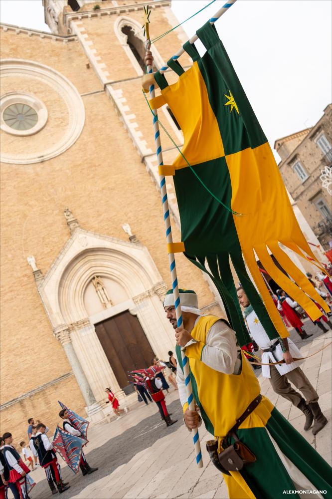 <div>Il corteo degli sbandieratori della Settimana Medioevale 2025 a Lucera, in costume storico con i colori giallo e verde, apre le celebrazioni e precede il Torneo delle Chiavi. La sfilata attraversa le vie del centro con spettacolari esibizioni, con la Cattedrale di Santa Maria Assunta sullo sfondo, custode della patrona della città.</div><div><br></div><div>Il <strong>Torneo delle Chiavi </strong>rappresenta uno dei momenti più identitari e attesi della Settimana Medioevale di Lucera, nonché uno degli eventi simbolo della tradizione cittadina. Inserito nel programma delle celebrazioni 2025, il Torneo si è svolto martedì 12 agosto, proseguendo una storia che affonda le proprie radici in oltre quarant’anni di rievocazione, giunta alla su...