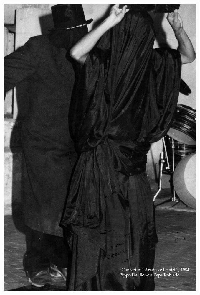 La fotografia in bianco e nero immortala i due attori Pippo Del Bono e Pepe Robledo in costume, nell'ambito della rassegna annuale “Aradeo e i Teatri” del 1984, alla seconda edizione con il titolo “Concertini”, un appuntamento con il teatro sperimentale che la compagnia Koreja, nata nel 1983 nel piccolo borgo salentino di Aradeo, porta avanti sin dall'anno della sua fondazione. Del Bono è attore e regista teatrale formatosi presso la scuola di Teatro di Savona dove incontrò Pepe Robledo, attore argentino proveniente dal “Libre Teatro Libre” (formazione teatrale attiva in Sud America negli anni Settanta che utilizzava la creazione collettiva come mezzo di espressione e di denuncia della dittatura in Argentina). Insieme i due attori, si trasferirono in Danimarca unendosi ...