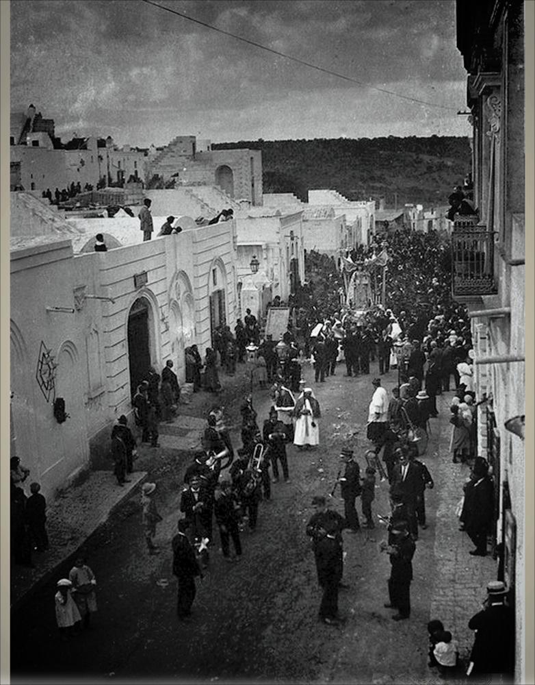 <div>Una foto storica, datata agli anni ’20, immortala la solenne processione con la statua durante la Festa Patronale di Ginosa in onore della Madonna del Rosario.</div><div>Questa festa, forte di una tradizione plurisecolare di oltre 260 anni, prende avvio nove giorni prima della prima domenica di ottobre con la novena nella Chiesa Matrice di Santa Maria del Rosario.</div><div>Il venerdì precedente la prima domenica di ottobre si svolge la suggestiva processione del quadro della Madonna per le vie del centro cittadino, accompagnata dalla Banda e dalla Bassa Musica di Ginosa. In questa occasione avviene la prima accensione ufficiale delle luminarie artistiche e, in piazza, l’immagine viene collocata sulla cassa armonica per la benedizione dei fedeli, a...