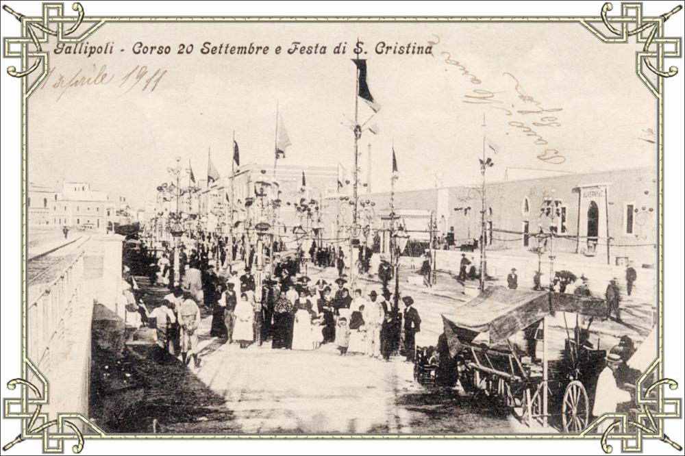 Fotografia storica dei primi anni del Novecento raffigurante Corso XX Settembre a Gallipoli allestito in occasione della festa patronale.
Il corso appare decorato con bandiere e banchetti, mentre una folla numerosa occupa lo spazio pubblico, si distinguono donne e bambini, insieme alla presenza di carabinieri.
Le persone ritratte, riconoscibili dagli abiti dell’epoca, volgono lo sguardo verso il fotografo.
La fotografia documenta la partecipazione popolare e l’organizzazione urbana della festa patronale nel primo XX secolo.

La festa patronale di Santa Cristina, protettrice della città; di Gallipoli, si svolge annualmente nei giorni 23, 24 e 25 luglio e rappresenta uno dei momenti più sentiti della vita religiosa, sociale e culturale cittadina. Secondo la tradizion...