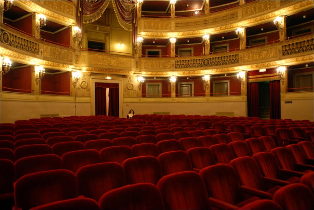 L'immagine è parte della campagna fotografica realizzata dalla fotografa Margherita Mirabella per Teatro Pubblico Pugliese, che con i suoi scatti ha ripreso le eleganti architetture e i rifiniti dettagli di alcuni dei più bei teatri pugliesi e di alcuni spettacoli teatrali portati in scena in questi ultimi anni. La foto, scattata dalla platea del Teatro Comunale Niccolò Piccini di Bari, restituisce uno scorcio degli eleganti palchi che dominano la sala. I lavori di costruzione del teatro furono avviati nel 1836 su progetto dell'architetto Antonio Niccolini e ultimati nel 1854; nello stesso anno fu inaugurato con l'allestimento del Poliuto di Gaetano Donizetti e nel 1855 venne dedicato al compositore barese Niccolò Piccini. Il Piccinni è il quarto teatro all'italiana più...