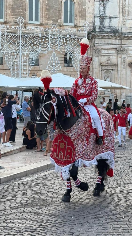 <div class="ql-editor"><div>Nell’immagine è ritratto uno dei cavalieri della storica Cavalcata in onore di Sant'Oronzo, momento centrale dei festeggiamenti patronali di Ostuni. Il cavaliere indossa l’elegante costume tradizionale, dai colori vivaci e dai dettagli curati, mentre il cavallo è finemente bardato con la caratteristica mantiglia rossa, simbolo distintivo della Cavalcata. La postura composta e solenne richiama il valore devozionale del corteo: non è solo una sfilata, ma un gesto di fede e appartenenza.</div><div><br></div><div> A Ostuni, ogni anno dal 25 al 27 agosto, si rinnova uno degli appuntamenti più sentiti dalla comunità: la Cavalcata in onore di Sant'Oronzo, solenne processione equestre che unisce fede, tradizione e...