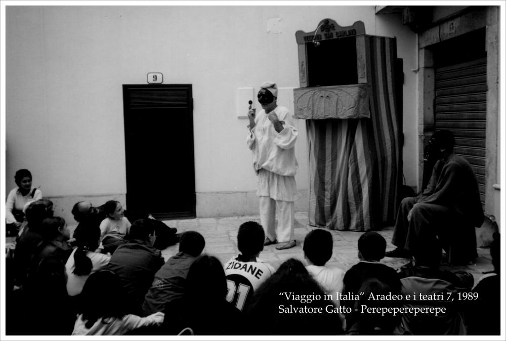 La fotografia in bianco e nero cattura un momento dello spettacolo di Salvatore Gatto, rappresentato nel 1989, nell'ambito della rassegna annuale “Aradeo e i Teatri”, un appuntamento con il teatro sperimentale che la compagnia Koreja, nata nel 1983 nel piccolo borgo salentino di Aradeo porta avanti sin dall'anno della sua fondazione. "Perepepereperepe" dell'attore napoletano Salvatore Gatto fu messo in atto l'1 agosto nel cortile del Castello Tre Masserie, una struttura residenziale degli inizi del XX secolo tra gli ulivi della campagna di Aradeo che divenne la sede operativa della compagnia. La rassegna, giunta alla settima edizione, si confermò come uno degli appuntamenti culturali estivi più attesi in Puglia, l'unico all'epoca di respiro internazionale, in programma ...