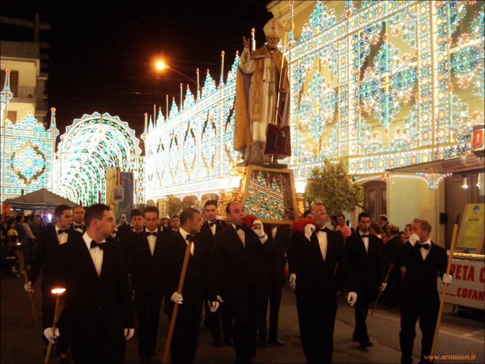 <div class="ql-editor"><div>Lo scatto fotografico cattura un momento topico della festa patronale di San Nicola Vescovo ad Aradeo in cui la statua del Santo viene portata in solenne processione per le vie cittadine illuminate da suggestive luci colorate.</div><div>La festa dedicata a San Nicola Vescovo, patrono di Aradeo, rappresenta un importante momento di devozione e partecipazione comunitaria. Le celebrazioni comprendono la novena liturgica nei giorni precedenti la festa, la processione per le vie del paese e numerosi eventi civili, tra cui manifestazioni musicali, culturali e artigianali.</div><div>La secolare devozione della comunità di Aradeo verso San Nicola, vescovo di Myra, trova una significativa testimonianza nella cappella di San Nicola di Myra, situat...