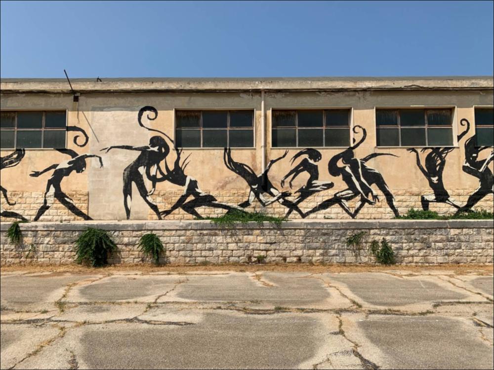 Iniziativa inaspettata è stata la realizzazione del grande murale "Metamor" grazie alla cooperazione tra l’illustratore croato Danijel Žeželj e lo street artist italiano Eron. Il grande murale decora i muri della nuova sede espositiva dell’ex Deposito Carburanti in Monopoli, esempio virtuoso di riqualificazione urbana che punta a diventare un hub di catalizzazione economica, culturale oltre che sociale.
L’opera “Metamor” è una danza lunga oltre 200 metri che rappresenta il ciclo della vita: dalle ombre di un grande uccello si inizia a definire un imponente airone bianco che con il suo volo elegante si trasforma in una danzatrice dalle linee tribali. La vorticosa danza si conclude con il volo di una colomba, simbolo dell'anima della ballerina. Il Racconto visivo si svilu...