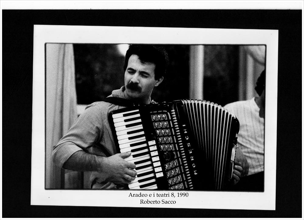 Nella fotografia in bianco e nero è rappresentato il musicista Roberto Sacco, ritratto mentre suona la fisarmonica in uno dei momenti di convivialità durante l'ottava edizione di "Aradeo e i Teatri", la rassegna annuale divenuta un appuntamento fisso con il teatro sperimentale che la compagnia Koreja nata nel 1983 nel piccolo borgo salentino di Aradeo portò avanti sin dall'anno della sua fondazione. Musicista e teatrante, conosciuto per le sue doti di fisarmonicista, Roberto Secchi, detto Sacco, divenne uno dei più apprezzati insegnanti della Scuola Popolare di Musica "Ivan Illich" di Bologna, per la quale insegnò fisarmonica spingendosi verso forme nuove di musica, come la computer music e tenne laboratori di "musica d'insieme", fino al 2011, anno della sua prematura s...