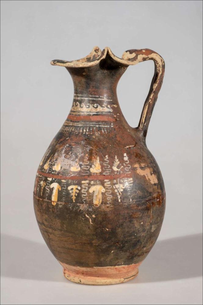 <div class="ql-editor"><div>L’oinochoe di Gnathia fu rinvenuta nel marzo 1935, in un terreno di proprietà del reverendo Stanca, in località Fontanella, all’interno di una sepoltura utilizzata più volte tra la fine del V e i primi decenni del III secolo a.C. Tra i materiali del corredo spicca questo vaso, decorato con motivi legati alla sfera del simposio e del banchetto. L’oinochoe presenta un ampio orlo trilobato, un collo leggermente ricurvo, un corpo ovoidale, un piede ad anello e un’ansa a bastoncello. La superficie è arricchita da una vivace decorazione sovraddipinta: sul collo si alternano motivi geometrici e onde correnti, mentre sulla parte superiore del corpo corre un tralcio di vite con grappoli e foglie, dipinti in ...
