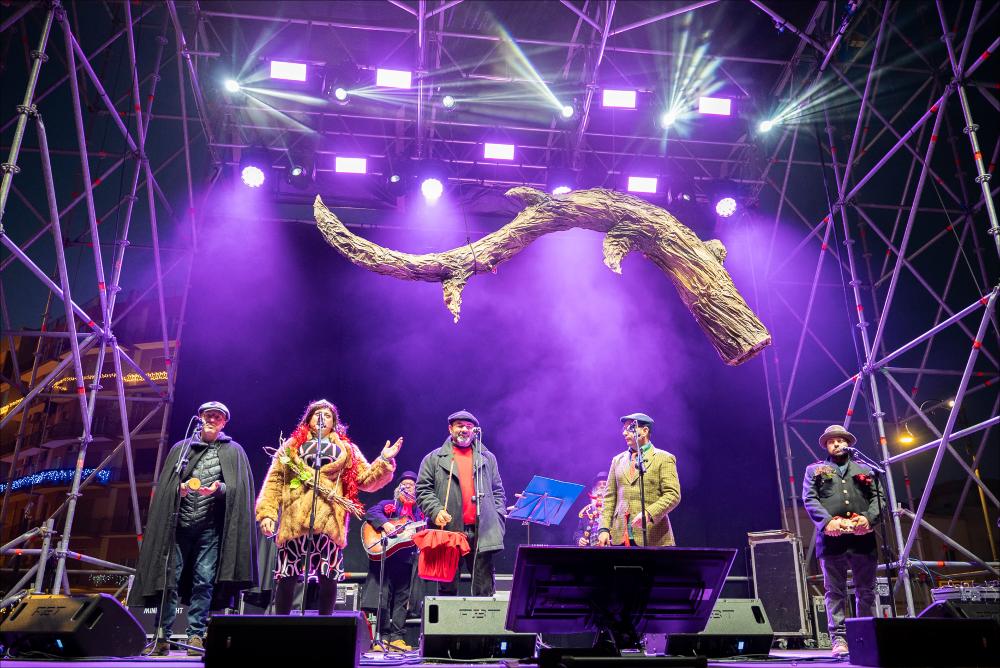<p>La fotografia ritrae l’energia e l’ironia di “Le Propaggini”, il tradizionale festival in vernacolo che ha aperto la 630^ edizione del Carnevale di Putignano il 26 dicembre. Sul palco di Largo Porta Nuova, otto gruppi di poeti irridenti hanno animato il pubblico con rime pungenti e satira locale, celebrando l’antica tradizione contadina che da secoli anima la città. L’immagine cattura il momento in cui i propagginanti, tra costumi colorati e sorrisi contagiosi, portano avanti la festa che unisce storia, divertimento e spirito di comunità.</p>...