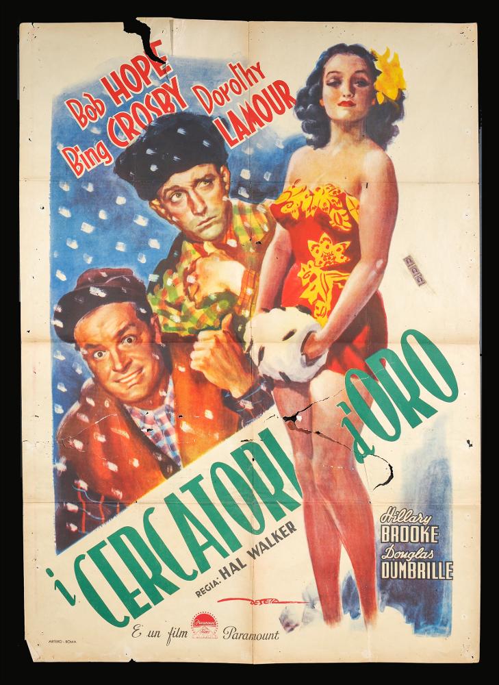 L'immagine riproduce uno dei manifesti conservati presso la Mediateca Regionale Pugliese (vedi Note). Si tratta di una delle versioni grafiche per il manifesto del film “I cercatori d’oro” del 1946 per la regia di Hal Walker a firma dell’illustratore Deseta (De Seta Enrico). Disegnatore e pittore italiano, noto come fumettista per giornali satirico-umoristici e periodici per ragazzi e soprattutto per la sua produzione di illustrazioni cinematografiche, De Seta realizza qui una composizione creata per mettere in risalto i personaggi del film, che accenna anche all'ambientazione fredda dell'Alaska. Con una pittura dai toni caldi e dalle pennellate sfumate, ritrae a figura intera la bellissima Dorothy Lamour, protagonista femminile, che spezza il titolo film posto in diago...