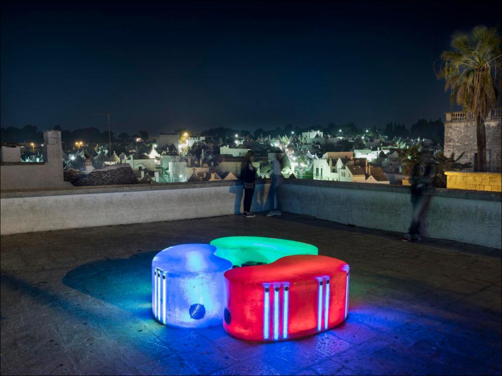 Lo scatto fotografico riprende l’installazione interattiva “Residence of Light and Music”, opera dei croati Igor Vasiljev e Marko Bolković, collocata presso il Belvedere di Alberobello. Una fusione di musica e luce composta da 3 panche di colori diversi che racchiudono suoni preselezionati di vari strumenti. Toccando la superficie della panca era possibile attivare suoni e luci, creando combinazioni sempre nuove di melodia e colore.
L’installazione è stata realizzata nell’ambito della seconda edizione del Life - Alberobello Light Festival 2017 che ha illuminato il centro cittadino e alcuni dei suoi luoghi più caratteristici dal 30 settembre all’8 ottobre.
Il Festival è organizzato da Lightcones e Agit - Associazione Giovani Imprenditori del Turismo, responsabili rispett...