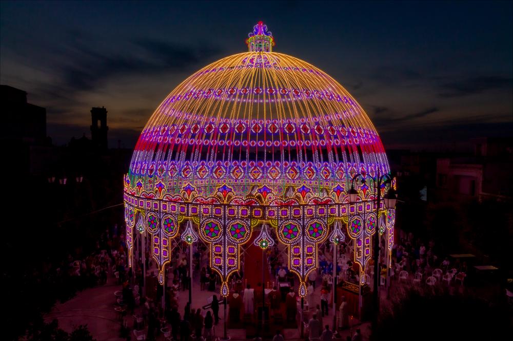Lo scatto fotografico ritrae la meravigliosa “Cassa Armonica”, nella piazza di Melendugno, che ospita famosi gruppi bandistici in occasione della Festa in onore del Santo Patrono Niceta.
La Festa Patronale di San Niceta Goto Martire, istituita nel 1740, si celebra nei giorni 15 e 16 Settembre a Melendugno in provincia di Lecce. Il rito religioso parte nove giorni prima della Festa, con delle celebrazioni eucaristiche presso la chiesa Madre e in forma esclusiva viene celebrata la santa messa in rito bizantino presso l’Abbazia di San Niceta situata in Melendugno sin dal 1167, riconosciuta appunto come uno dei più importanti riferimenti storici del territorio.
Il giorno della vigilia della Festa, come da tradizione pluricentenaria, al termine della Santa Messa, i fedeli ac...