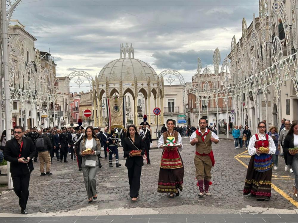 L’immagine ritrae il corteo dell’“Offerta della Cera”, tradizione secolare che si svolge il 28 settembre a Monte Sant’Angelo, vigilia della solennità di San Michele Arcangelo. Protagonisti della processione sono i figuranti in abiti tradizionali del gruppo folkloristico “La Pacchianella”, che portano in offerta caratteristici cesti di cera e sfilano insieme all’Amministrazione Comunale verso il Santuario di San Michele Arcangelo. Il dono della cera rappresenta un gesto simbolico di devozione e di affidamento dell’intera comunità all’Arcangelo ed è spesso accompagnato dall’accensione di un cero votivo durante la Santa Messa celebrata nella suggestiva Grotta del Santuario. La celebrazione eucaristica, talvolta presieduta da alte autorità religiose, costituisce uno dei mom...