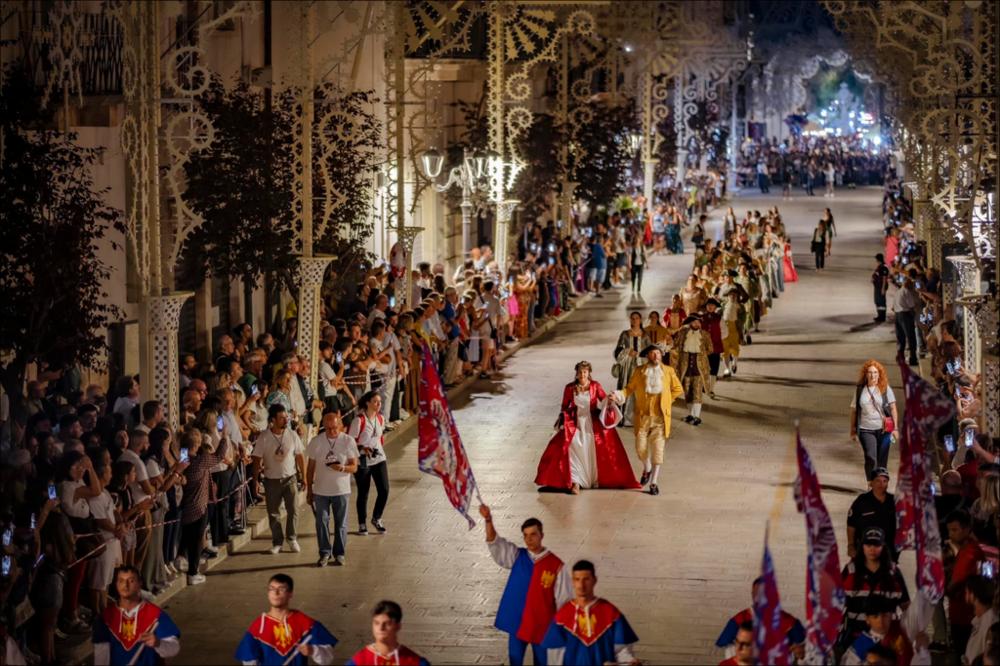 La fotografia ritrae il corteo storico, organizzato per celebrare la Festa di Sant'Oronzo, Patrono di Turi, mentre sfila per le strade della città, tra l’entusiasmo vibrante dei presenti.
La Festa Patronale di Sant’Oronzo, che si celebra il 25 e 26 agosto, è molto più di una ricorrenza religiosa: è un intreccio di fede, tradizione e spettacolo capace, ogni anno, di coinvolgere l’intera comunità.
Simbolo indiscusso della festa è il maestoso Carro Trionfale: un’imponente torre lignea, trainata da sei mule, che riaccompagna il Santo dalla grotta fino al cuore del paese, tra giochi di luce, musica festosa e una folla gremita di emozione.
Il 25 agosto è dedicato alla Processione alla Grotta. Il busto di Sant’Oronzo parte dalla Chiesa Madre e viene accompagnato in preghiera f...