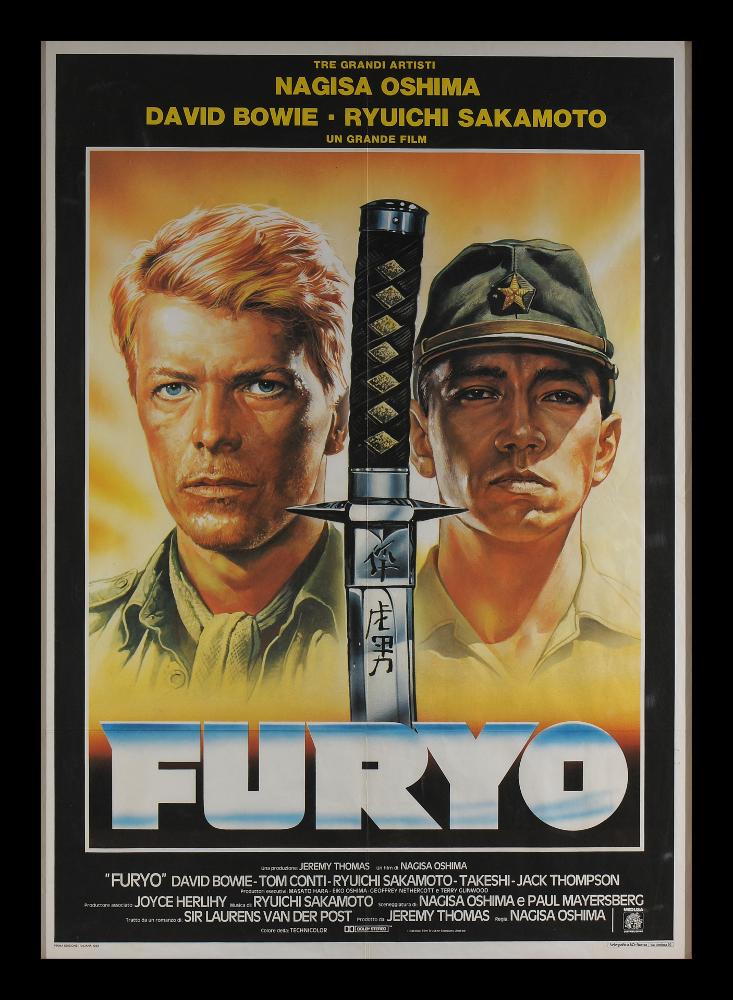 Manifesto realizzato dal famoso illustratore e pittore del cinema, Renato Casaro. Dominano la scena i due ritratti di Davis Bowie e Ryuichi Sakamoto separati dall'elsa di una katana giapponese. Trattandosi d'una produzione britannico-nipponico-neozelandese, la pellicola possiede due titoli originali, uno in giapponese ed uno in inglese, simili tra loro "Merry Christmas, Mr. Lawrence", ma in alcune edizioni europee, fra cui quella italiana, è stato ridenominato "Furyo", traducibile dal giapponese come "prigioniero di guerra". Il manifesto originale è conservato nell’Archivio della Mediateca Regionale Pugliese....