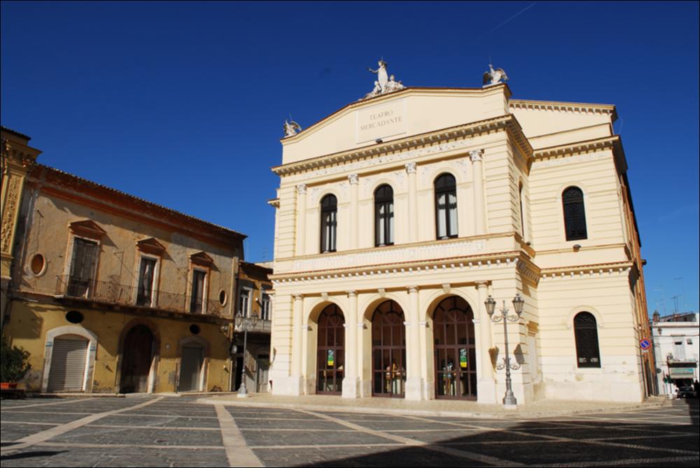 L'immagine è parte della campagna fotografica realizzata dalla fotografa Margherita Mirabella per Teatro Pubblico Pugliese, che ha ripreso nei suoi scatti le eleganti architetture e i rifiniti dettagli di alcuni dei più bei teatri pugliesi e alcuni degli spettacoli teatrali portati in scena in questi ultimi anni. L'autrice cattura il prospetto principale di Teatro Saverio Mercadante, situato in Piazza Giacomo Matteotti a Cerignola. Oggi gestito in collaborazione con il Teatro Pubblico Pugliese, la struttura teatrale fu inaugurata nel 1868. La storia del teatro inizia nel 1854, quando fu proposta la necessaria costruzione di un teatro cittadino. Dopo diverse proposte che risultarono piuttosto onerose, la scelta ricadde sull'architetto Leopoldo Vaccaro che presentò un pro...