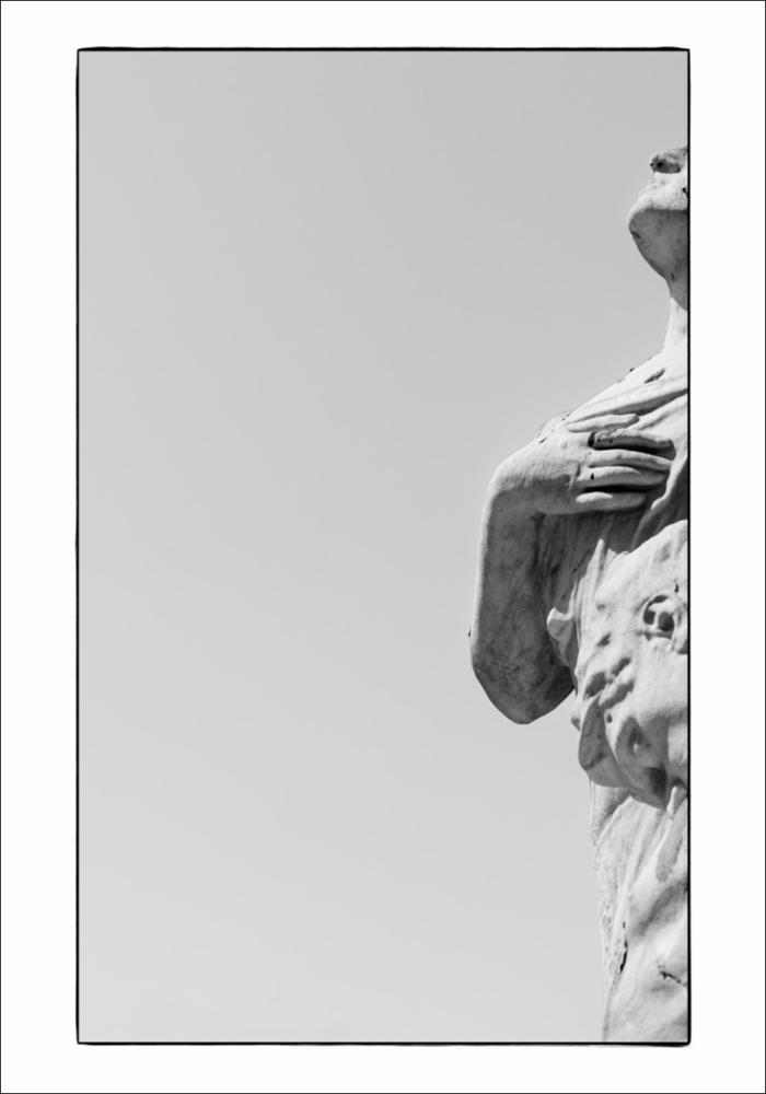 L'immagine in bianco e nero esalta un bellissimo dettaglio del Monumento ai Caduti di Trani, dedicato ai concittadini caduti nella Prima Guerra Mondiale. Il monumento a cippo fu realizzato nel 1923 da Antonio Bassi, scultore originario di Trani formatosi tra Roma e Vienna. Tutto in pietra bianca di Trani, è collocato nella Villa Comunale, in prossimità del centro storico, un esempio affascinante di giardino all'italiana misto a giardino all'inglese, che si affaccia sul mare. Il monumento è di tipo a cippo, sui cui basamenti sono evidenti alcuni bassorilievi e il bellissimo gruppo scultoreo, sempre in pietra locale, raffigurante l'Allegoria del sacrificio del soldato per la Patria. La fotografia è stata esposta nel Salone degli Affreschi del Palazzo Ateneo di Bari per la...