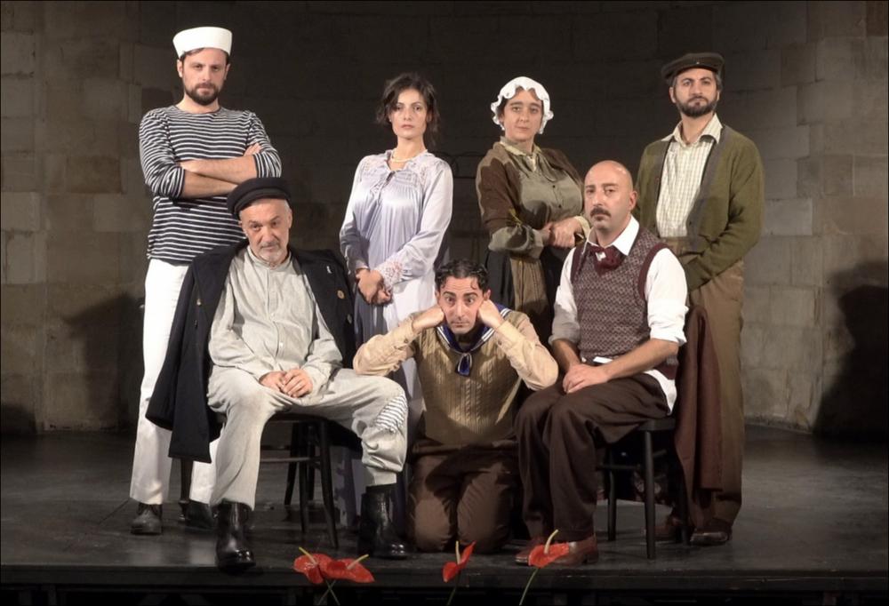 Lo scatto ritrae l’intero cast, appartenente alla Compagnia Diaghilev, nel “L’uomo, la bestia e la virtù allestito sotto la regia di Paolo Panaro, una commedia grottesca dai toni libertini del 1919, dove vengono fuori i temi cari a Pirandello: l’ipocrisia, l’identità e le maschere che l’uomo indossa per nascondere la sua vera natura.  L’opera racconta di tre figure: il Marito, un violento e rozzo capitano di marina, che avendo abbandonato la donna per rifarsi una famiglia a Napoli, appare agli occhi della gente con la maschera della Bestia. La moglie, che rappresenta la Virtù, moglie fedele e devota alla famiglia e, infine, l’amante di lei, il Professore, che rappresenta l’uomo, che sotto l’aspetto distinto nasconde la relazione con la Signora Perella.  
Questo spettaco...