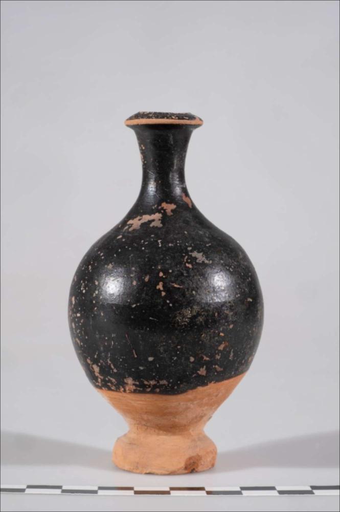 <div class="ql-editor"><div>L’unguentario in ceramica a vernice nera faceva parte del corredo della tomba n. 3, rinvenuta nel 1900 da Cosimo De Giorgi durante i lavori per la costruzione della Banca d’Italia, in piazza Sant’Oronzo. La tomba conteneva la sepoltura di una giovane di circa quindici anni, individuata attraverso l’analisi dei resti ossei. L’unguentario, insieme ad altri due esemplari e a una pelike, era deposto sulle gambe dell’inumata, probabilmente come parte del corredo personale o rituale. Il vaso presenta un orlo estroverso, un collo stretto e un corpo di forma ovoidale, poggiante su un basso piede. È rivestito di vernice nera, ad eccezione del fondo e del piede.</div></div>