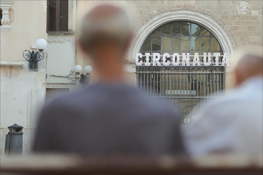 <div>Lo scatto ritrae l’iconica insegna del Circonauta Festival 2024, installata sulla facciata del Sedile monumentale in piazza Salandra, nel cuore di Nardò (LE).</div><div>Il Circonauta Festival Internazionale del Circo Contemporaneo ha celebrato la sua X edizione dal 6 al 14 luglio 2024 nel centro storico di Nardò (Lecce). In dieci anni il festival ha ospitato compagnie internazionali, presentando numerose anteprime nazionali e regionali.</div><div>Il programma, articolato su due weekend, ha trasformato la città in un palcoscenico diffuso con spettacoli di circo e musica, incontri letterari, tavole rotonde, workshop e mostre fotografiche.</div><div>La decima edizione, dedicata al tema #FOU! in omaggio a Franco Basaglia nel centenario della nascit...