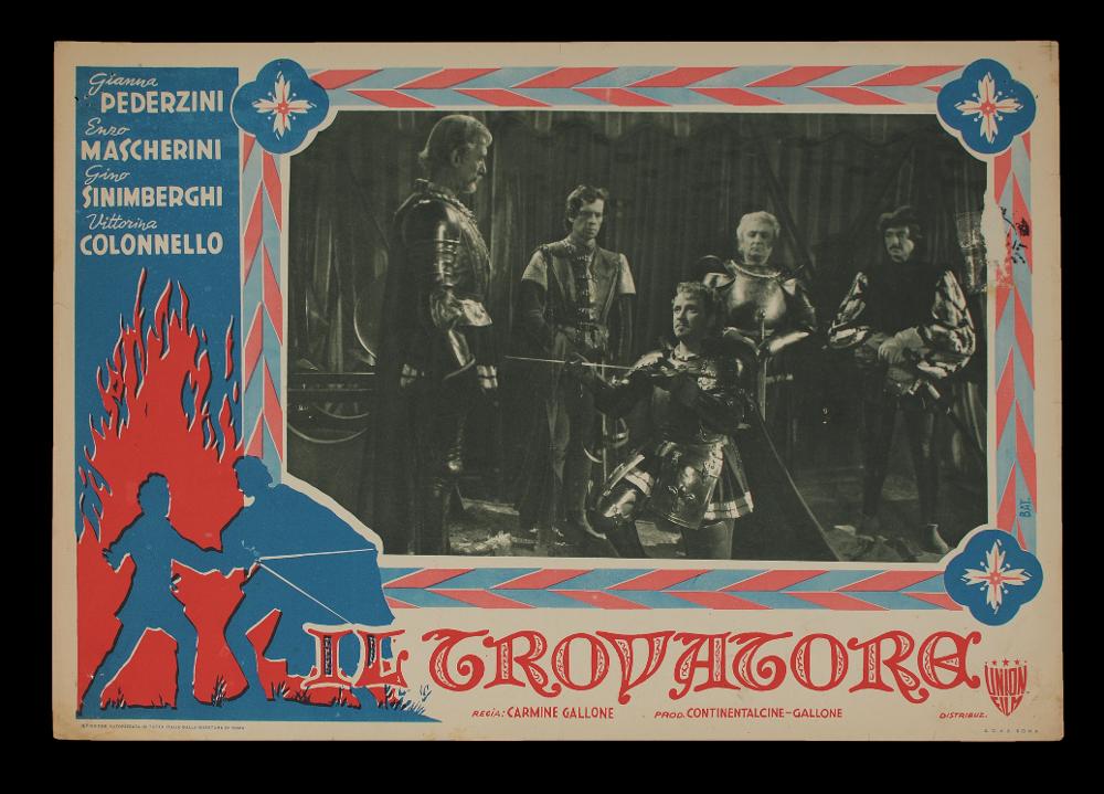 L'immagine riproduce uno dei manifesti conservati presso la Mediateca Regionale Pugliese (vedi Note). Si tratta di uno dei soggetti per la fotobusta del film italiano "Il trovatore", la cui illustrazione è a firma dell'illustratore Bat. (Giovanni Battaglia). L'artista concepisce una illustrazione molto decorativa, dai forti elementi ornamentali, soprattutto sulla greca a tinte rosso e blu, che corrono intorno all'immagine in bianco e nero, tratta dal film. A sinistra, una rappresentazione invece molto stilizzata in cui rappresenta un momento di duello con silhouette blu che fuoriescono dalle fiamme rosse....