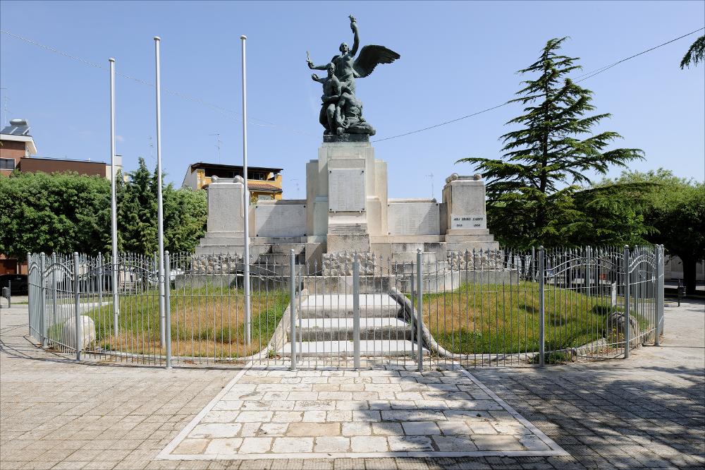 L'immagine digitale cattura il Monumento ai Caduti di Cassano delle Murge. Posizionato al centro di Piazza Dante Alighieri, è realizzato in bronzo, marmo e pietra come un'ara sul cui basamento sono riportate le lastre con incisioni dei concittadini caduti nelle due guerre mondiali. Degne di nota sulla sommità le statue in bronzo, con al centro l'Allegoria della Vittoria, realizzate dalla Fonderia / Marmeria Chiurazzi su progetto artistico dello scultore Vitantonio De Bellis. L'artista è annoverato tra i casi più interessanti a livello pugliese, autore di altri monumenti pugliesi come quello di Rutigliano e Carbonara, tanto da poterlo definire uno specialista del genere, attività fortunata che porterà lo stesso artista a dedicarsi, negli anni '60-'70, al restauro e reint...