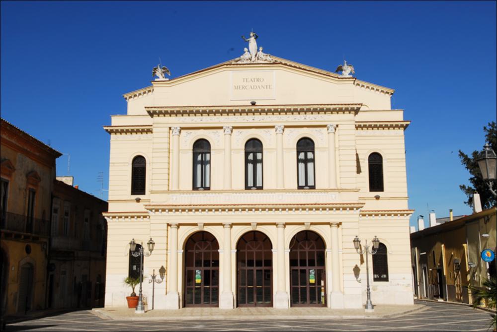 L'immagine è parte della campagna fotografica realizzata dalla fotografa Margherita Mirabella per Teatro Pubblico Pugliese, che ha ripreso nei suoi scatti le eleganti architetture e i rifiniti dettagli di alcuni dei più bei teatri pugliesi e alcuni degli spettacoli teatrali portati in scena in questi ultimi anni. L'autrice cattura il prospetto principale di Teatro Saverio Mercadante, situato in Piazza Giacomo Matteotti a Cerignola. Oggi gestito in collaborazione con il Teatro Pubblico Pugliese, la struttura teatrale fu inaugurata nel 1868. La storia del teatro inizia nel 1854, quando fu proposta la necessaria costruzione di un teatro cittadino. Dopo diverse proposte che risultarono piuttosto onerose, la scelta ricadde sull'architetto Leopoldo Vaccaro che presentò un pro...