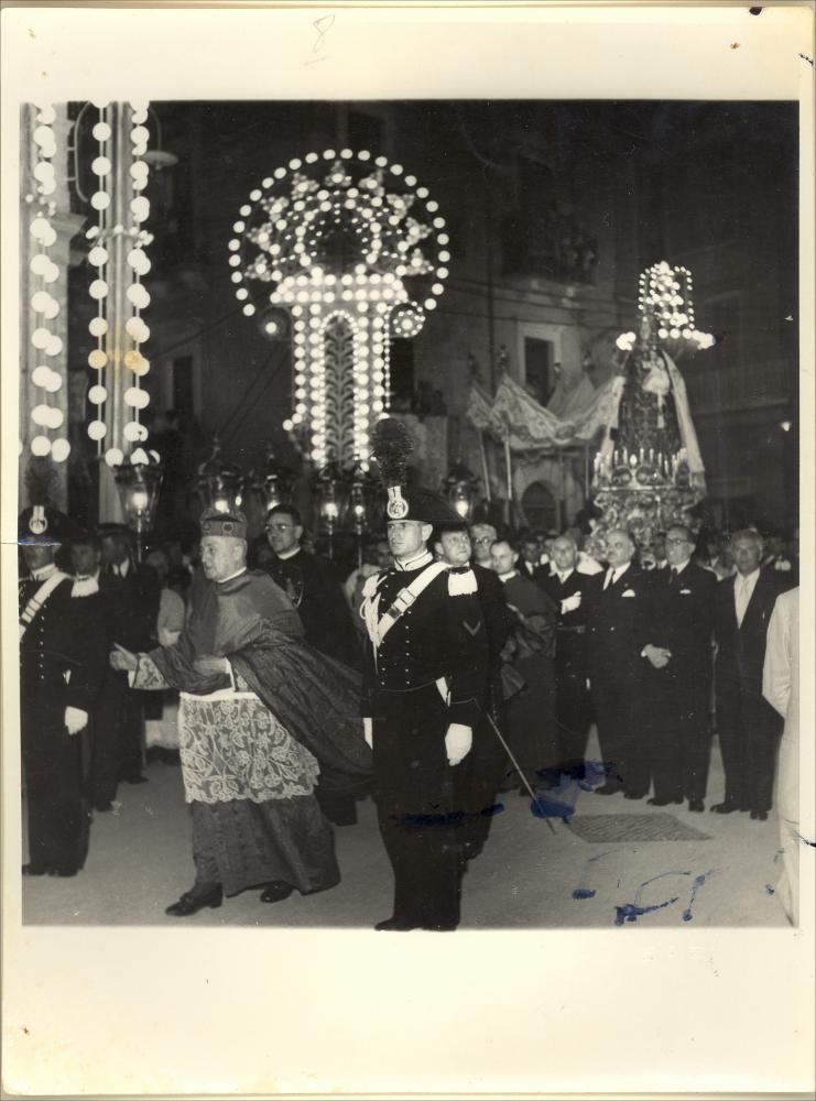 <div class="ql-editor"><div> La digitalizzazione di questa foto storica del 1962 cattura un momento solenne della Processione con la statua della Madonna del Carmine che sfila accompagnata da rappresentanti di istituzioni ecclesiastiche e civili.</div><div> La festa patronale di Santa Maria del Carmine a Noicattaro, celebrata ogni anno il 16 luglio e nel fine settimana successivo, rappresenta uno degli appuntamenti più significativi per la comunità, sia dal punto di vista religioso sia culturale. È un momento di intensa partecipazione collettiva, che unisce devozione, tradizione e vita sociale.</div><div>Le giornate di festa sono scandite da tre solenni processioni, tra sabato, domenica e lunedì, durante le quali la statua della Madonna del Carmine v...