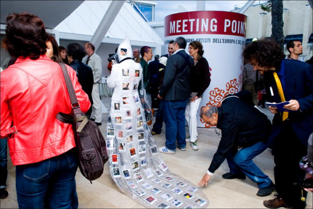 L'immagine digitale documenta un momento della "Biennale dei Giovani Artisti dell'Europa e del Mediterraneo" che, nella sua XIII edizione, fu ospitata in Puglia, a Bari, dal 22 al 31 maggio 2008 negli spazi della Fiera del Levante. La Biennale è considerata la più importante vetrina in Europa e nel Mediterraneo per la creatività delle giovani generazioni. Regione Puglia e dall'Associazione Internazionale BJCEM e realizzata dal Teatro Pubblico Pugliese, la Biennale ha dato così spazio ad una visione multidisciplinare, multiforme e internazionalizzata dell'arte contemporanea attraverso creazioni di musica, arti visive, teatro, video, arti applicate, letteratura e gastronomia. Scattata a luce ambiente in uno degli spazi della Fiera, la fotografia rende l'istante di una per...