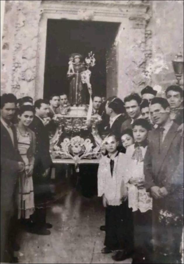 <div class="ql-editor"><div>Fotografia del 1951 che documenta la celebrazione di Sant’Antonio da Padova a Minervino di Lecce. Il simulacro del santo viene portato in processione attraverso la porta secondaria della chiesa, poiché il portale principale era in restauro.</div><div><br></div><div>A Minervino di Lecce, Sant’Antonio da Padova è protagonista di celebrazioni tutto l’anno: a febbraio con un triduo e la Messa per il ritrovamento della lingua del santo, a giugno con la novena e la processione del 13, a luglio con la <em>Peregrinatio</em> nelle case delle famiglie, e ad agosto con la grande festa patronale (8-10) che permette il ritorno degli emigranti. La processione culmina in Piazza Umberto I con Messa cantata, concerto delle bande e ...
