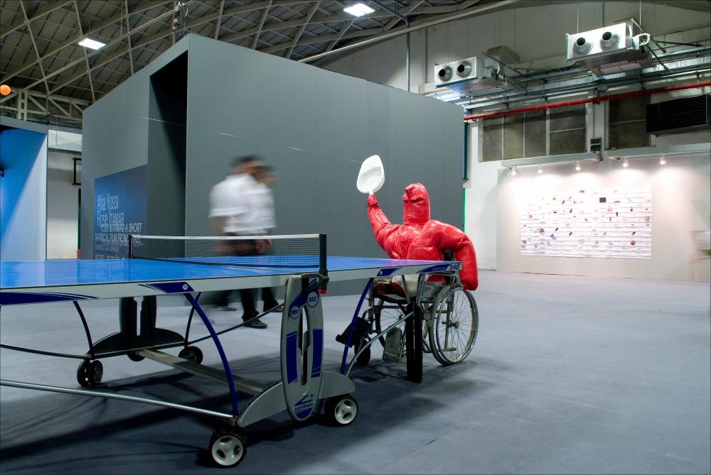 L'immagine digitale documenta un momento della "Biennale dei Giovani Artisti dell'Europa e del Mediterraneo" che, nella sua XIII edizione fu ospitata in Puglia, a Bari, dal 22 al 31 maggio 2008 negli spazi della Fiera del Levante. La Biennale è considerata la più importante vetrina in Europa e nel Mediterraneo per la creatività delle giovani generazioni. Voluta da Regione Puglia e dall'Associazione Internazionale BJCEM e realizzata dal Teatro Pubblico Pugliese, la Biennale ha dato così spazio ad una visione multidisciplinare, multiforme e internazionalizzata dell'arte contemporanea attraverso creazioni di musica, arti visive, teatro, video, arti applicate, letteratura e gastronomia. Scattata a luce ambiente in uno degli spazi della Fiera, la fotografia rende una delle i...