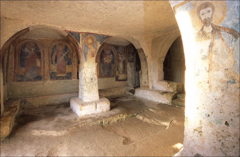 L'immagine digitale rappresenta un particolare, immortalato dal fotografo pugliese Carlos Solito, dell'interno della chiesa-grotta di San Nicola, sita nel cuore del villaggio rupestre di Casalrotto a Mottola. Scavata nella roccia nel IX secolo la chiesa si trova nei pressi della “via tarantina”, antica strada consolare. Accanto l'ingresso, probabilmente destinata alla sepoltura del benefattore che aveva patrocinato la costruzione della chiesa, è posta una nicchia sormontata da un arco, mentre una scala metallica ricavata nella roccia consente l'accesso all'interno, diviso in tre navate. La chiesa presenta uno dei cicli di affreschi più interessanti per qualità e per stato di conservazione della Puglia (sono stati effettuati i restauri nel 1972) tanto da essere conosciut...