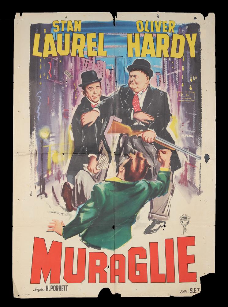 L'immagine riproduce uno dei manifesti conservati presso la Mediateca Regionale Pugliese (vedi Note). Si tratta del manifesto del film "Muraglie", a firma di M. Seba. È una delle moltissime composizioni realizzate per la comicità di Stanlio & Ollio, il duo iconico tra i più amati della storia del cinema. L'artista rivela uno stile narrativo moderno e composto in cui spiccano i ritratti fedeli e realistici dei due attori  in una composizione che risalta la comicità elementare della coppia artistica, nota al grande pubblico per le loro gag semplici ed esilaranti, adatte a ogni tipo di età. Le loro mimiche facciali, il linguaggio del loro corpo si impongono in questa scena/gag urbana, dai colori pop....