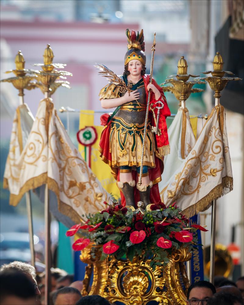 <div class="ql-editor"><div>La foto ritrae il <strong>simulacro di San Trifone</strong> durante la processione per le vie di Adelfia. Il Santo è portato in spalla dai devoti tra ali di folla.</div><div><br></div><div>La Festa di San Trifone di Adelfia, conosciuta come “La Regina delle Feste”, è tra le celebrazioni patronali più spettacolari della Puglia. Si svolge ogni anno nei primi giorni di novembre e culmina il 10 novembre con la solenne processione del simulacro di San Trifone, preceduta dalla simbolica consegna delle chiavi della città. Protagoniste indiscusse sono le monumentali luminarie, che da oltre un secolo trasformano la piazza in un suggestivo scenario di luce, e la celebre gara pirotecnica diurna, considerata tra le più...