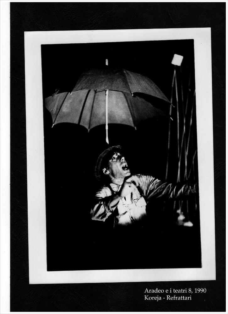 La fotografia in bianco e nero è un momento dello spettacolo "Refrattari", rappresentato nel 1990 dal Teatro Koreja durante l'ottava edizione di "Aradeo e i Teatri", un appuntamento con il teatro sperimentale che la compagnia nata nel 1983 nel piccolo borgo salentino di Aradeo porta avanti sin dall'anno della sua fondazione. Proposto per la prima volta proprio in quest'occasione, la rappresentazione teatrale diretta da Salvatore Tramacere è liberamente ispirata al "Woyzeck" di Georg Büchner e ai suoi personaggi. La sceneggiatura si basa sul concetto che i refrattari sono dei folli che vivono in un luogo chiuso, senza aria né luce. Metaforicamente vivono il vuoto in un mondo vicino al crollo, dove le certezze sono perse. L'unico modo per sentirsi vivi nel mondo è agitars...