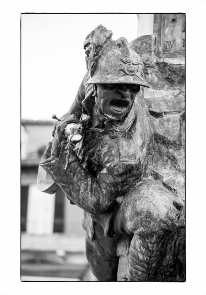 L'immagine digitale mostra un particolare del Monumento ai Caduti ad Ascoli Satriano, opera dello scultore bolognese Giulio Barberi. Racchiuso da una cancellata in ferro battuto, su un doppio gradone, vi è un blocco in marmo sul quale si erge un gruppo bronzeo, sul quale a sua volta si innalza un obelisco su cui sono state inserite delle foglie di palma in bronzo. Il gruppo scultoreo consta di due protagonisti: a sinistra, come si può vedere dal dettaglio, un bersagliere è ritratto nel momento di avanzamento alla carica con moschetto e baionetta innestata, mentre sulla destra vi è un fante colpito che cade avendo tra le braccia la bandiera. I due personaggi sembrano sporgersi da una parete rocciosa. Sui lati dell'obelisco sono presenti delle targhe bronzee: una in facci...
