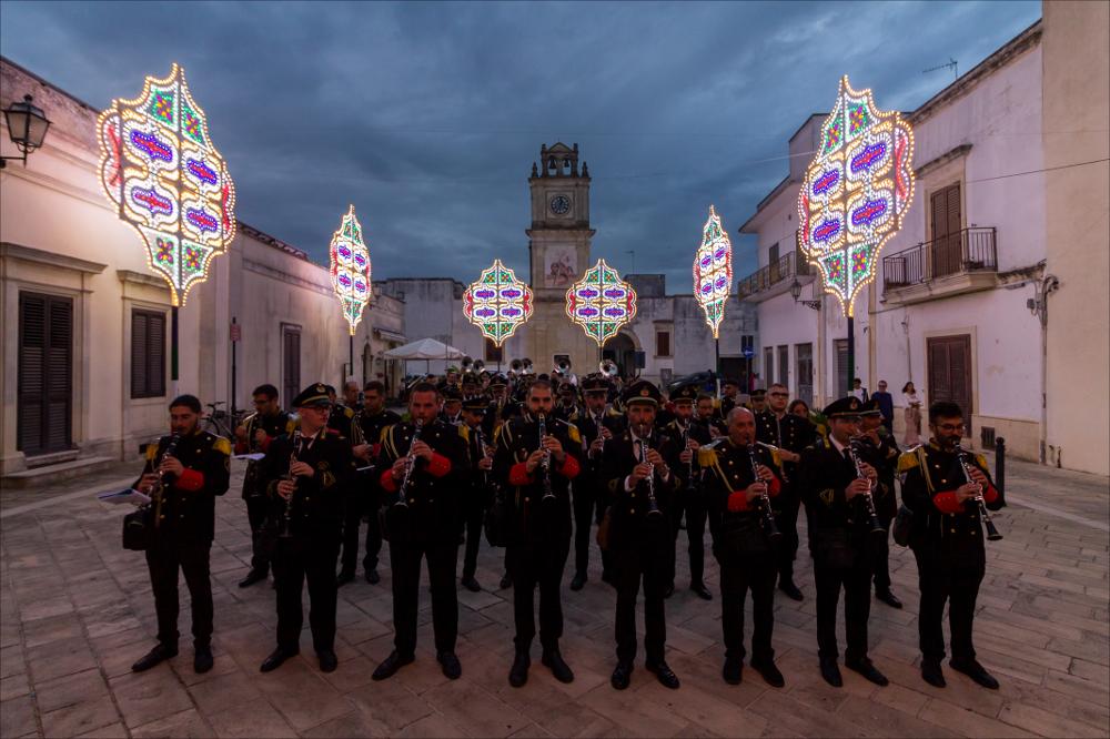 In questo scatto fotografico è protagonista una delle rinomate bande che allietano a suon di musica le vie cittadine di Melendugno in occasione della Festa Patronale di San Niceta.
La Festa di San Niceta Goto Martire, istituita nel 1740, si celebra nei giorni 15 e 16 Settembre a Melendugno in provincia di Lecce. Il rito religioso parte nove giorni prima della Festa, con delle celebrazioni eucaristiche presso la chiesa Madre e in forma esclusiva viene celebrata la santa messa in rito bizantino presso l’Abbazia di San Niceta situata in Melendugno sin dal 1167, riconosciuta appunto come uno dei più importanti riferimenti storici del territorio.
Il giorno della vigilia della Festa, come da tradizione pluricentenaria, al termine della Santa Messa, i fedeli accompagnati da un...