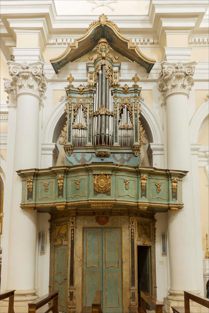 L'organo rappresentato nell'immagine digitale è collocato nella Collegiata dedicata a Ognissanti di Mesagne. L’edifico fu con ogni probabilità riedificato sotto il periodo di Roberto d’Angiò nel 1322, ristrutturato nel Quattrocento e poi nel Cinquecento, attualmente si presenta come una chiesa totalmente barocca. La facciata divisa in tre ordini, suddivisi da paraste, presenta nicchie con statue di santi, mentre un enorme frontone corona la parte superiore con al centro lo stemma dell’Università. Il progetto iniziale fu opera dell’architetto Francesco Capodieci, poi subentrò Salvatore Miccoli e infine l’ingegnere Giuseppe Palmieri con il capomastro Giuseppe Fasano di Ostuni. Al 1769 si data l’intervento del napoletano Nicola Carletti che diede uniformità decorativa all’...